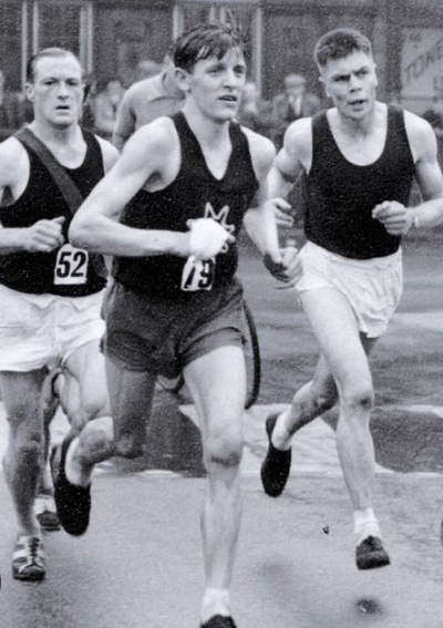 Black and white image of three men taking part in a running race on the street
