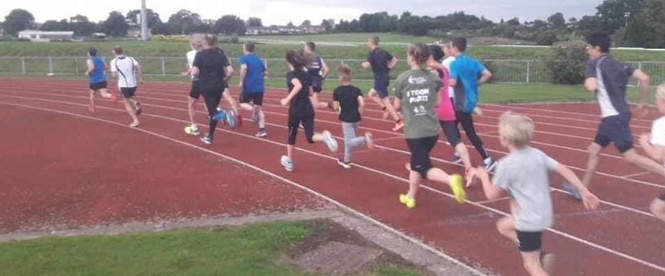 Large group of runners on a running track. The group are a mix of ages and genders