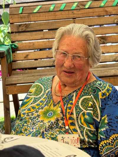 Oder lady in bright colours smiling at the camera wearing a 100 today badge