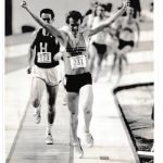 Black and white image of male athlete holding his arms aloft and he crosses the finish line