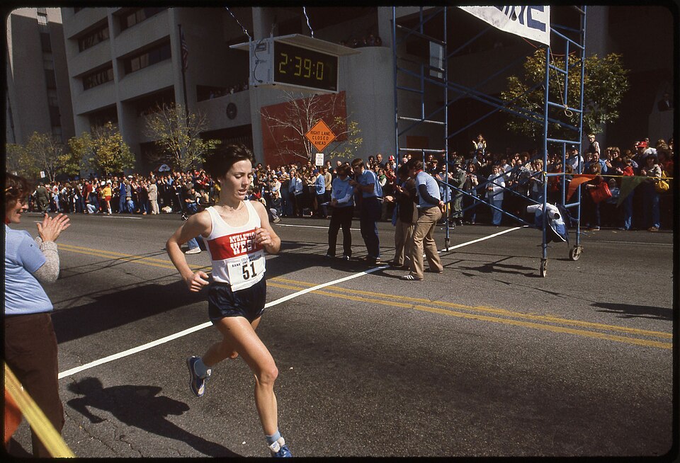 Female athlete crosses the finish line in a city marathon in a time of 2::39:00 with crowds of spectators watching