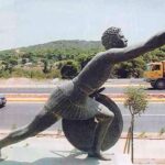 Bronze statue of a male runner of Ancient Greece holding out and olive branch in his right hand and resting on his shield with his left hand