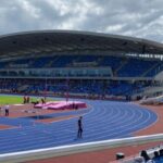 A view of Alexander Stadium showing the curve of the track onto the home straight, pole vault, and stand