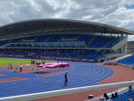 A view of Alexander Stadium showing the curve of the track onto the home straight, pole vault, and stand